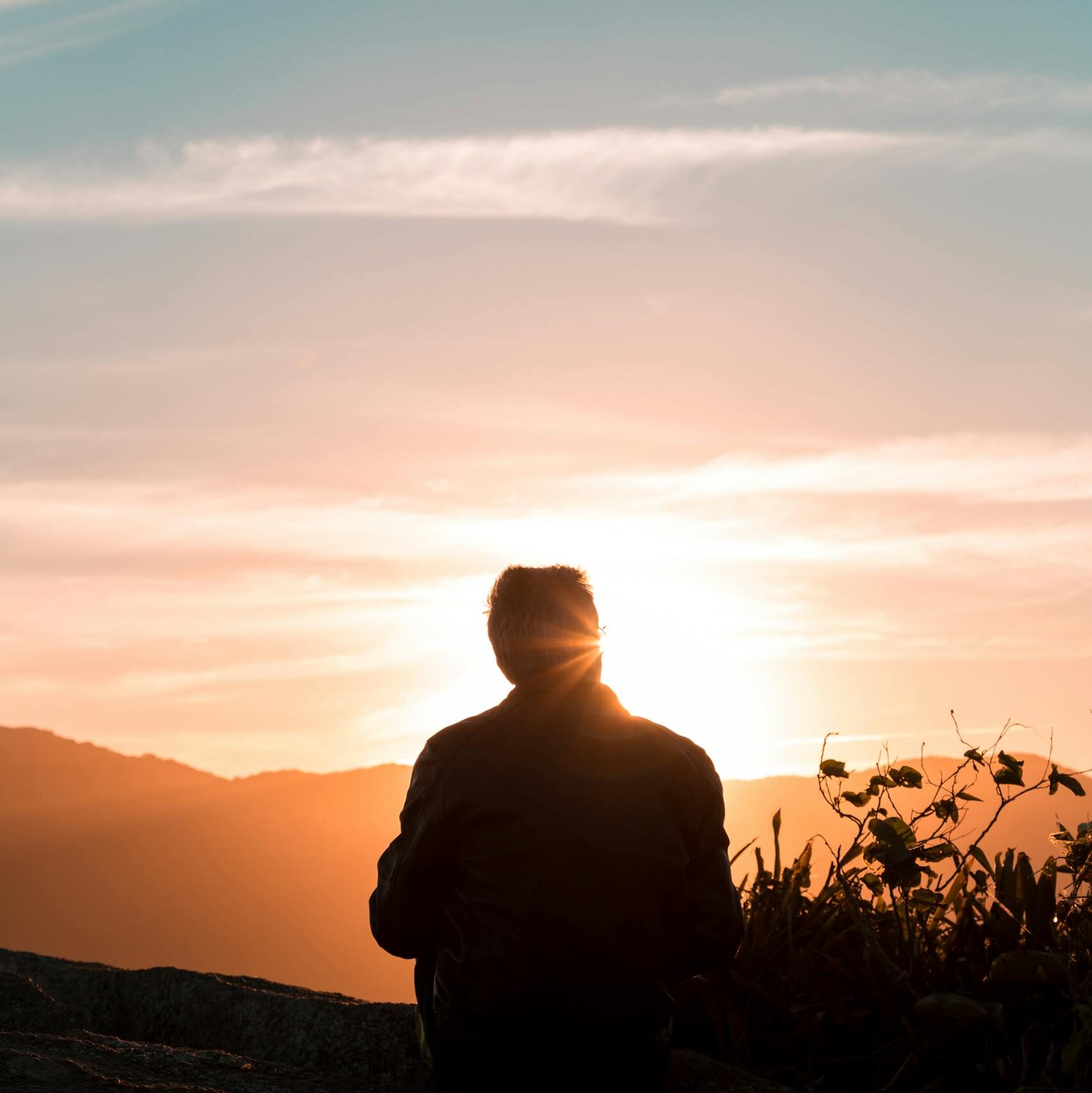 Silhouette of Person Sitting and Facing Mountain during Sunset