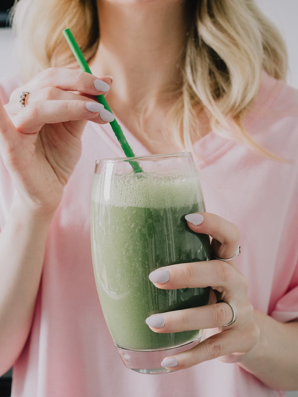 Close-up of a woman in a pink shirt holding a green smoothie for a healthy diet.