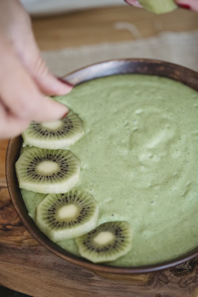 Nutritious green smoothie bowl beautifully topped with fresh kiwi slices in a wooden bowl.